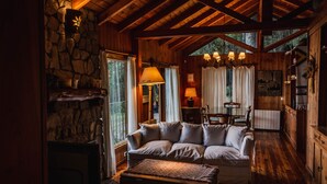 A cozy cabin interior with a stone fireplace, wooden ceiling beams, a sofa, and a dining area. - Beatiful Cabin in Bariloche (San Carlos de Bariloche)