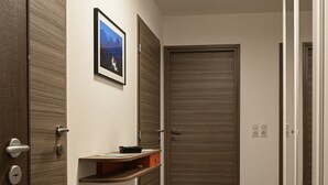 Un pasillo con una puerta de madera, un cuadro en la pared y un pequeño estante con un objeto negro.