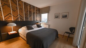 Un dormitorio moderno con una cama grande, dos lámparas de noche, suelo de madera y una ventana con vistas.