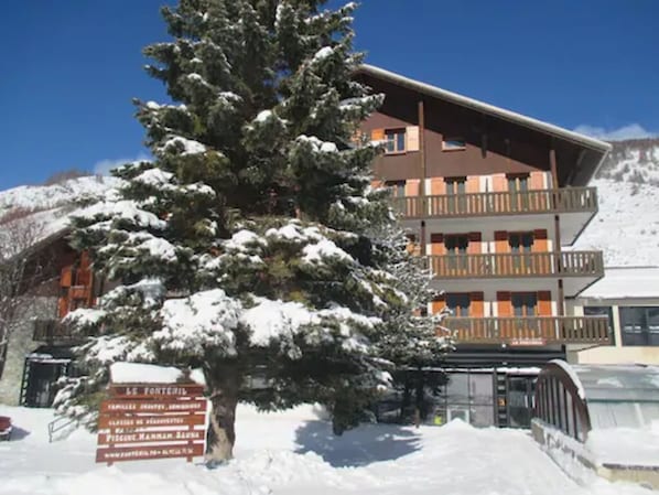 A multi-story building with balconies, surrounded by snow-covered trees. - Le Fontenil (Abriès-Ristolas)