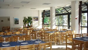 A spacious dining area with multiple tables and chairs, large windows allowing natural light, and a tiled floor. - Le Fontenil (Abriès-Ristolas)