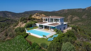 Ein modernes, zweistöckiges Haus mit Pool, umgeben von üppiger Vegetation und Hügeln.