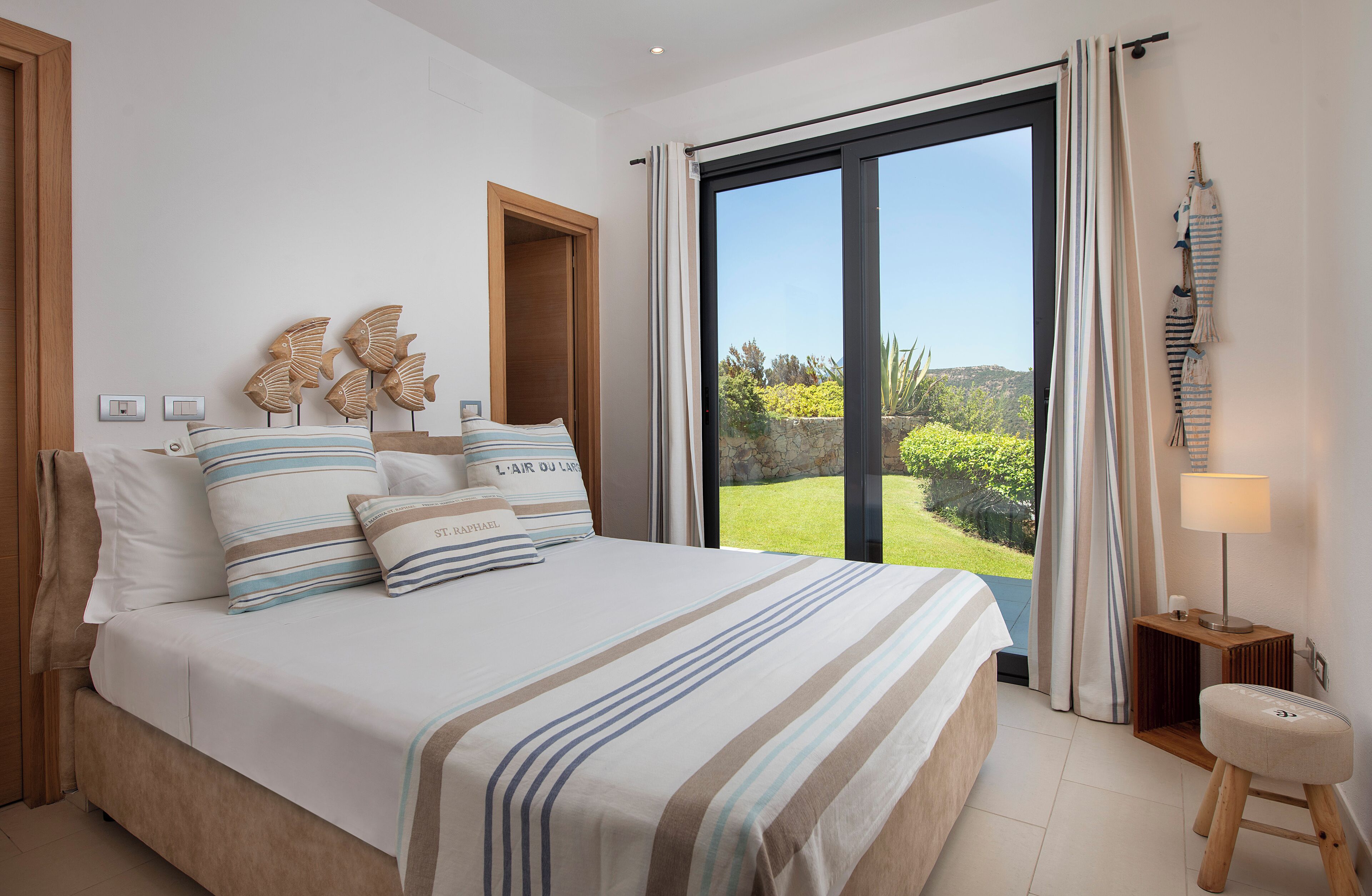 A bedroom with a large bed, a view of the outdoors, and a small stool.