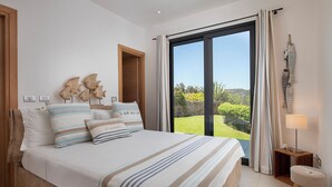 Ein Schlafzimmer mit einem großen Bett, Blick ins Freie und einem kleinen Hocker.