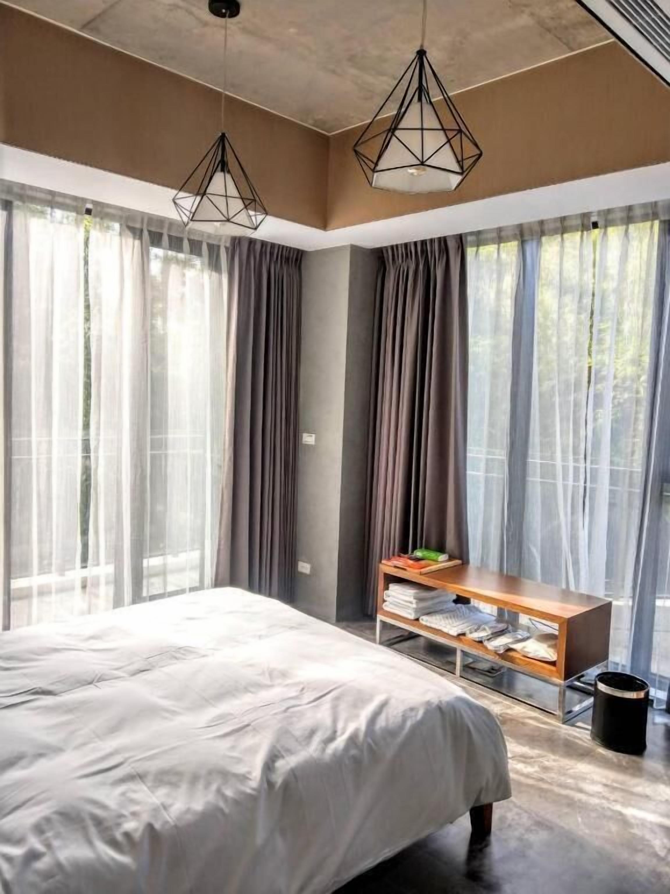A modern bedroom with a large bed, a wooden bench, and sheer curtains.