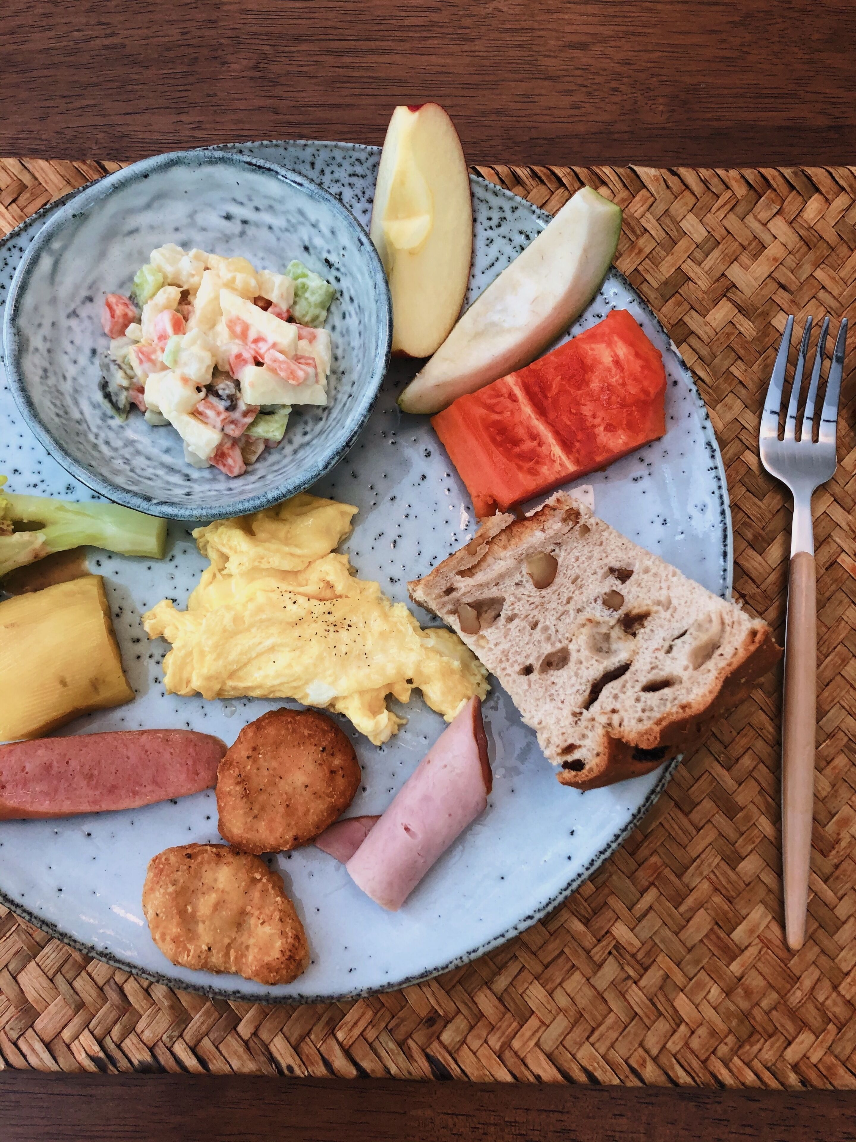En tallerken med røræg, pølser, ristet brød og en skål med frugtsalat.