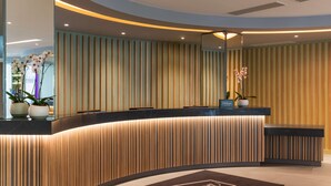 A modern hotel reception area with a curved reception desk, vertical wooden paneling, and a large mirror. - Hampton by Hilton London Ealing (London)