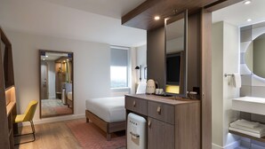 A modern hotel room with a bed, a small fridge, a mirror, a TV, and a bathroom with a sink and towel rack. - Hampton by Hilton London Ealing (London)