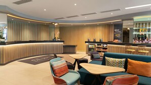 A modern lounge area with a curved reception desk, seating arrangements, and a bar. - Hampton by Hilton London Ealing (London)