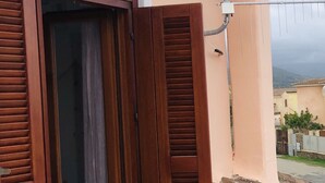 A balcony with a wooden door open, revealing a tiled floor and a view of the surrounding neighborhood. - Fantastico Budoni Tauanella ARGO01 (Budoni)