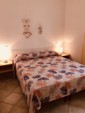 A bedroom with a bed covered in a floral-patterned bedspread, two bedside tables with lamps, and a wall decoration above the bed.