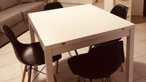 A living room with a white table, black chairs, a grey sofa, a small white cabinet, and a flat-screen TV mounted on the wall. - Fantastico Budoni Tauanella ARGO02 (Budoni)