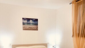 A bedroom with a bed, two bedside tables, a nightstand, a wall-mounted picture, and a sheer curtain. - Fantastico Budoni Tauanella ARGO02 (Budoni)