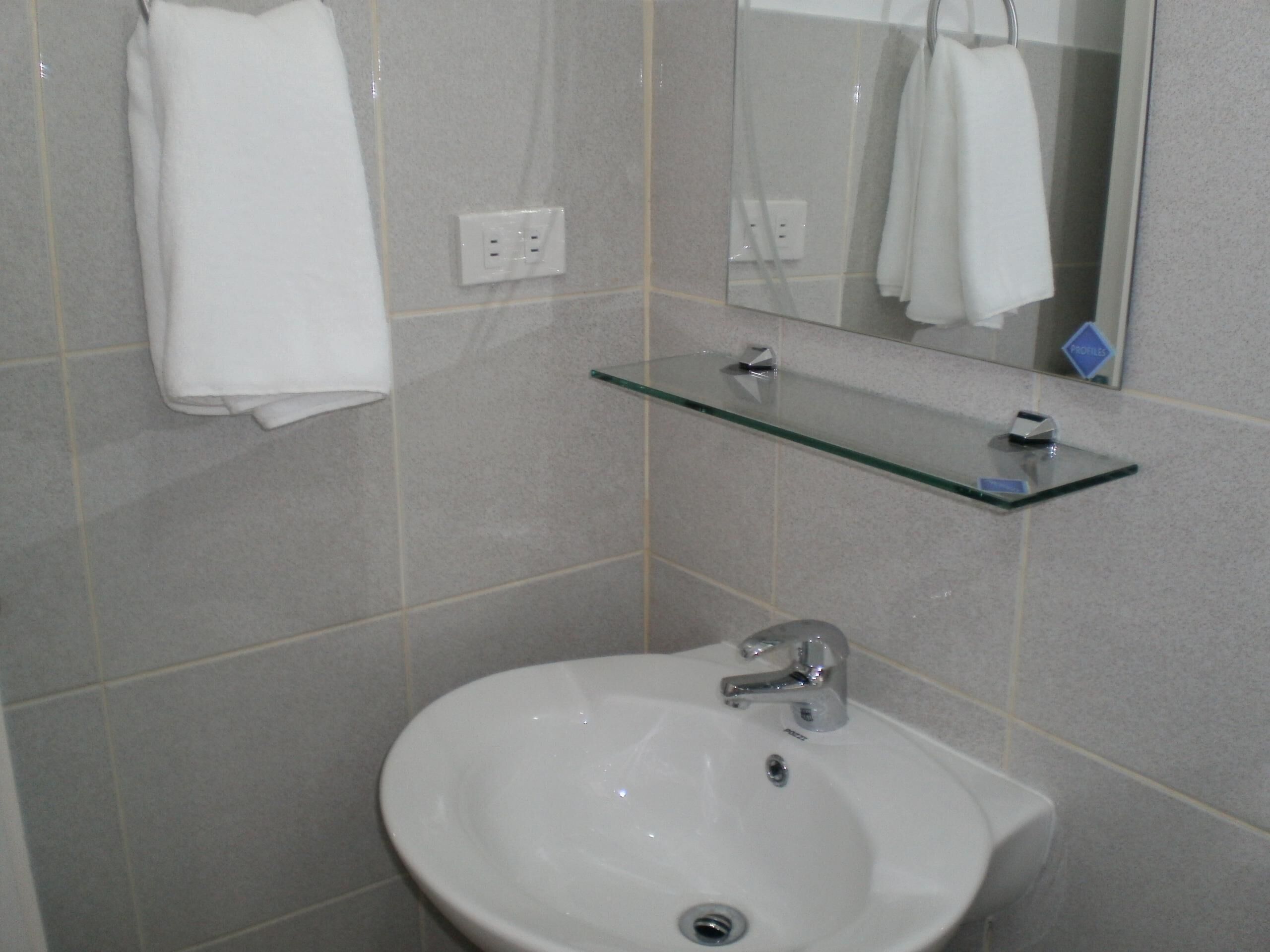 A bathroom with a white sink, a glass shelf, and a mirror.