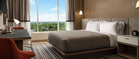 Habitación de hotel con una cama grande, un escritorio, una silla y vistas a la ciudad.