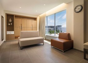 A modern living room with a beige sofa, a brown armchair, and a large window offering a view of a building under construction.