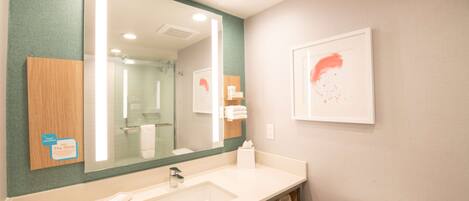 Un baño con un espejo grande, un lavabo, un inodoro y una obra de arte enmarcada en la pared.