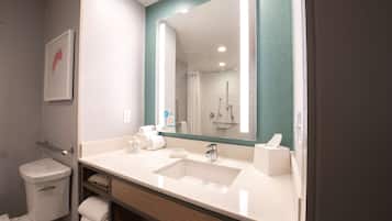 A modern bathroom with a large mirror, white sink, and a shower visible in the background.