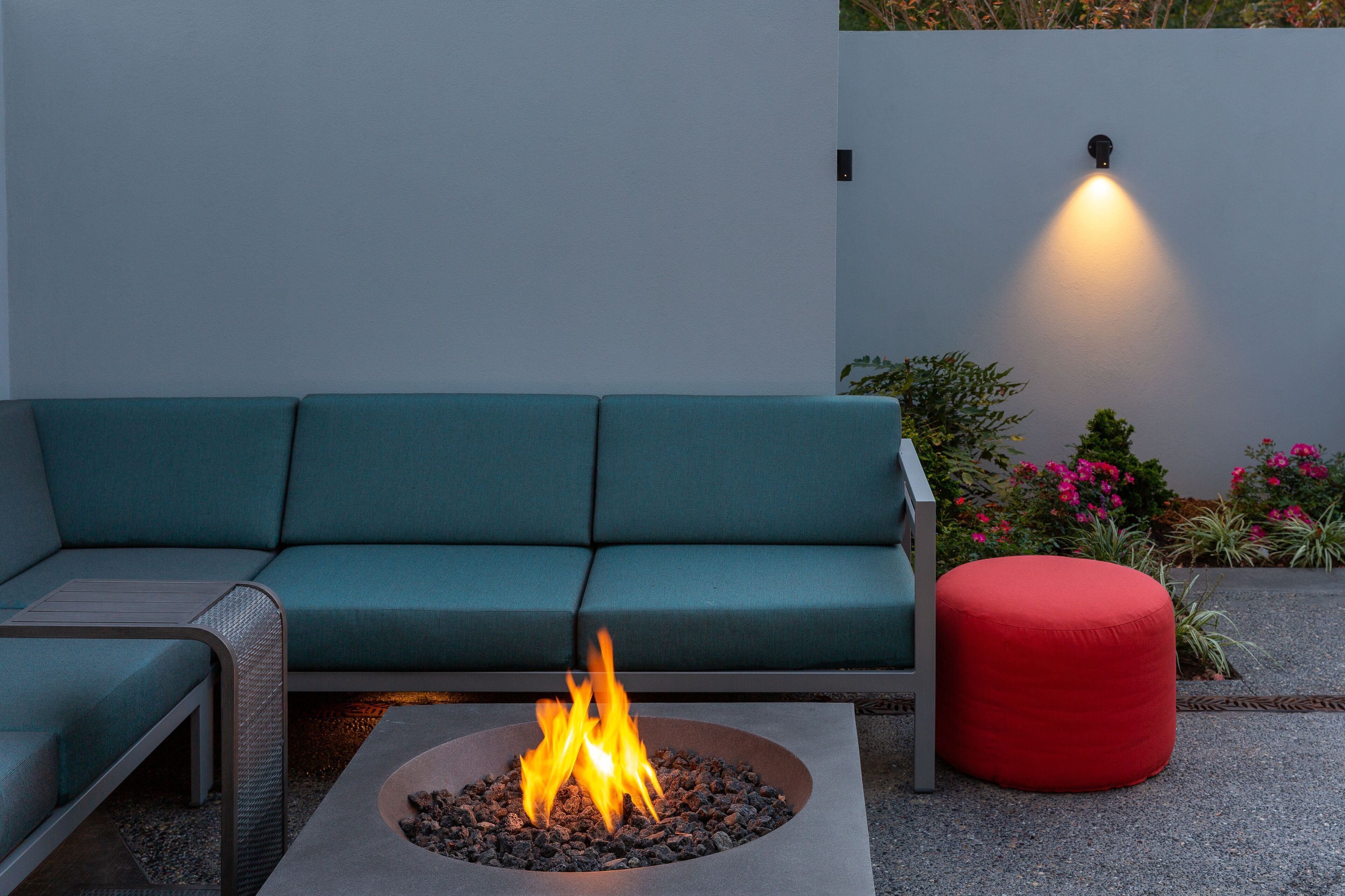 Un espace extérieur moderne, aménagé avec des sièges, un foyer et un pouf rouge.