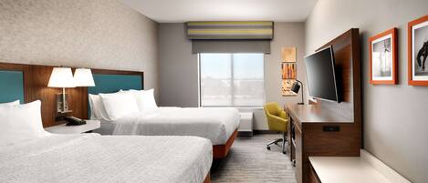 Habitación de hotel con dos camas, un escritorio, un televisor y una ventana con vistas a la ciudad.