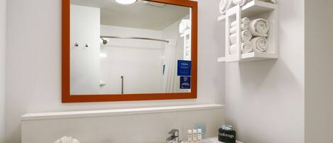 A bathroom with a large mirror, a sink, and a towel rack with neatly rolled towels.