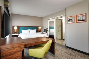 A hotel room with a bed, desk, chair, TV, lamps, and two framed pictures on the wall.