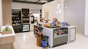 Interior de una cafetería con mostrador, estanterías llenas de granos de café y un refrigerador.