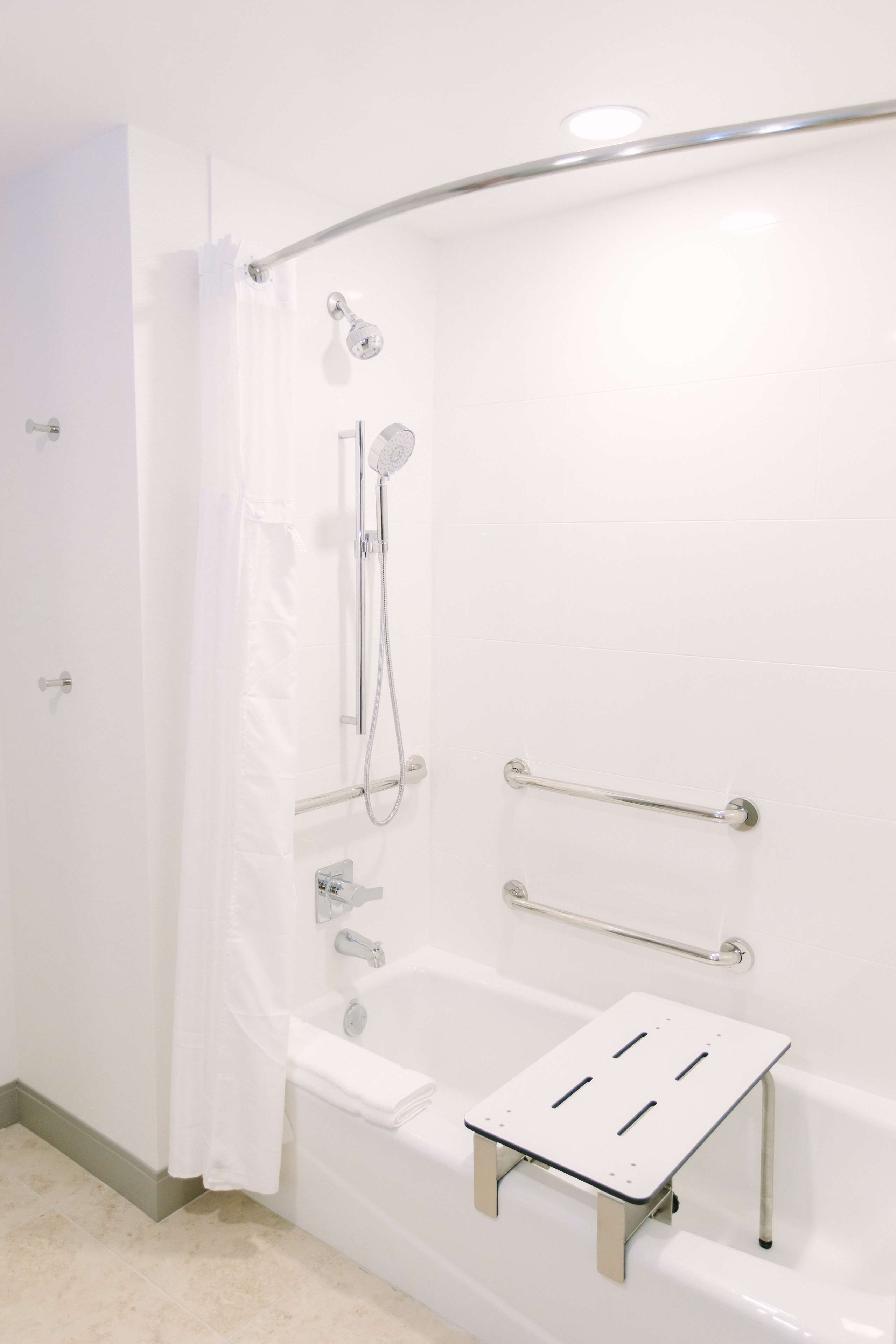 Une salle de bain blanche avec une douche, des barres d’appui et un petit tabouret.