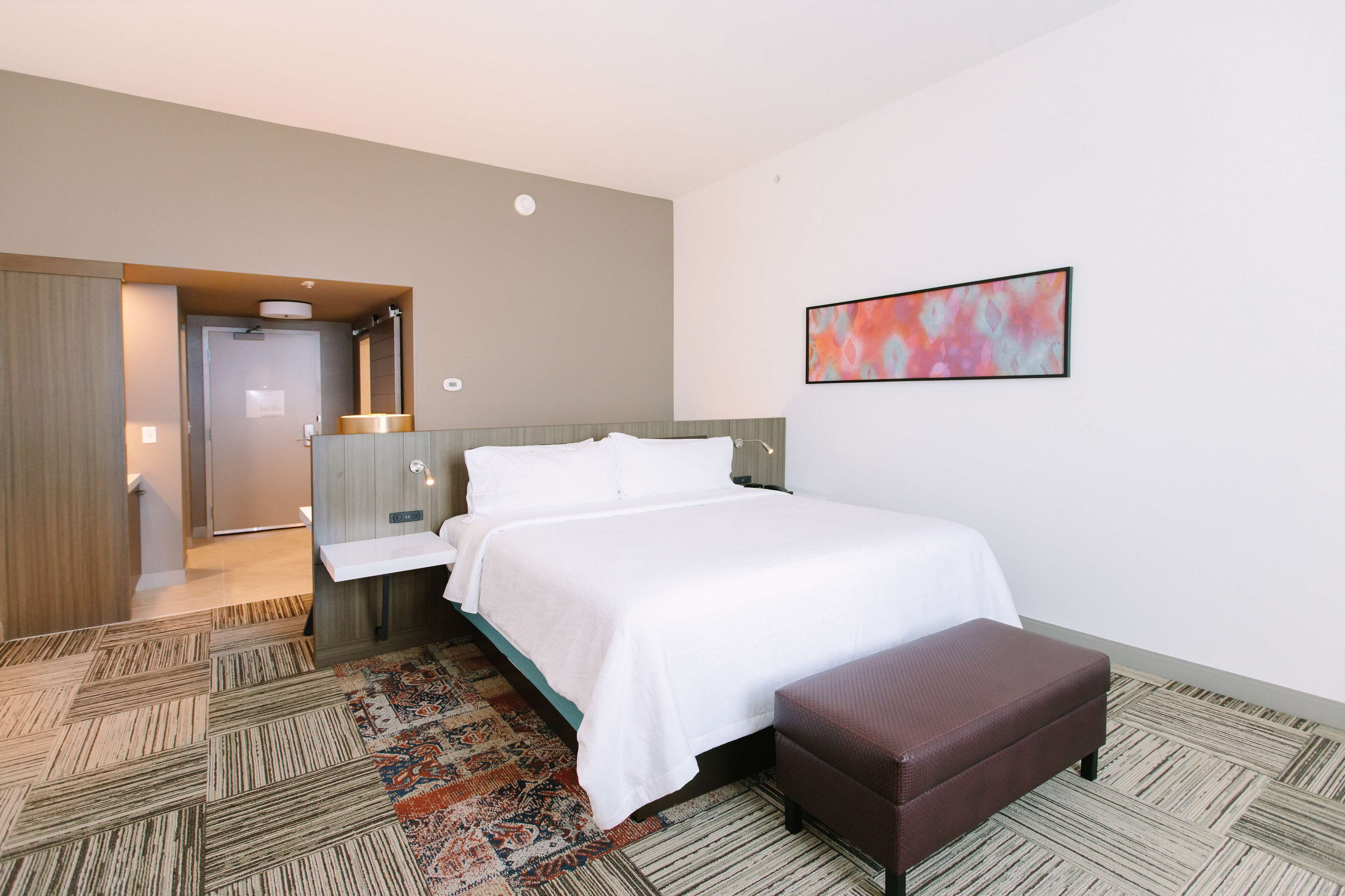 Una camera d'albergo con un letto, una panca, un bagno e un quadro appeso al muro.