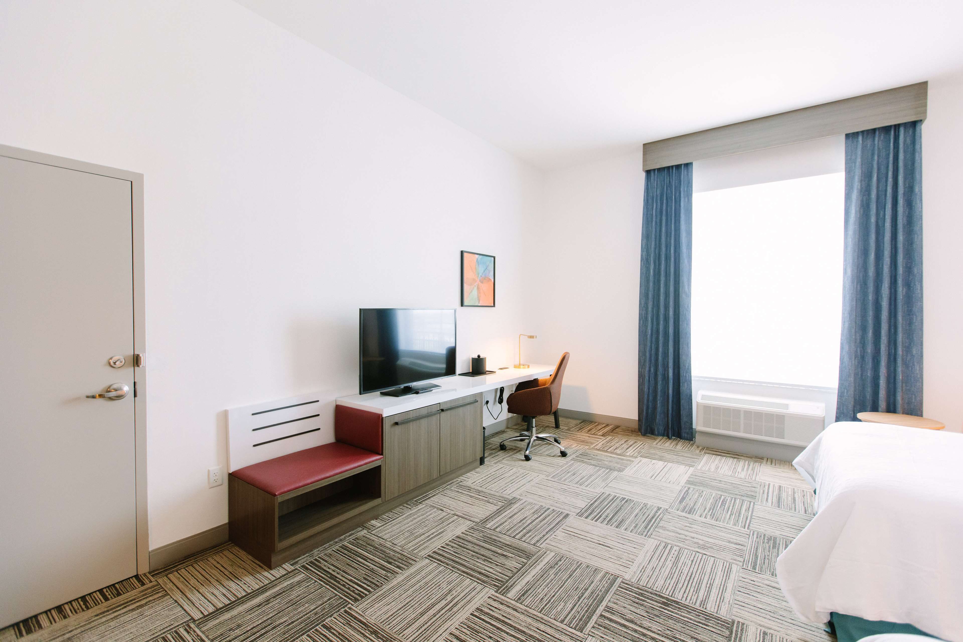 A hotel room with a bed, a desk with a chair, a television, and a window with curtains.