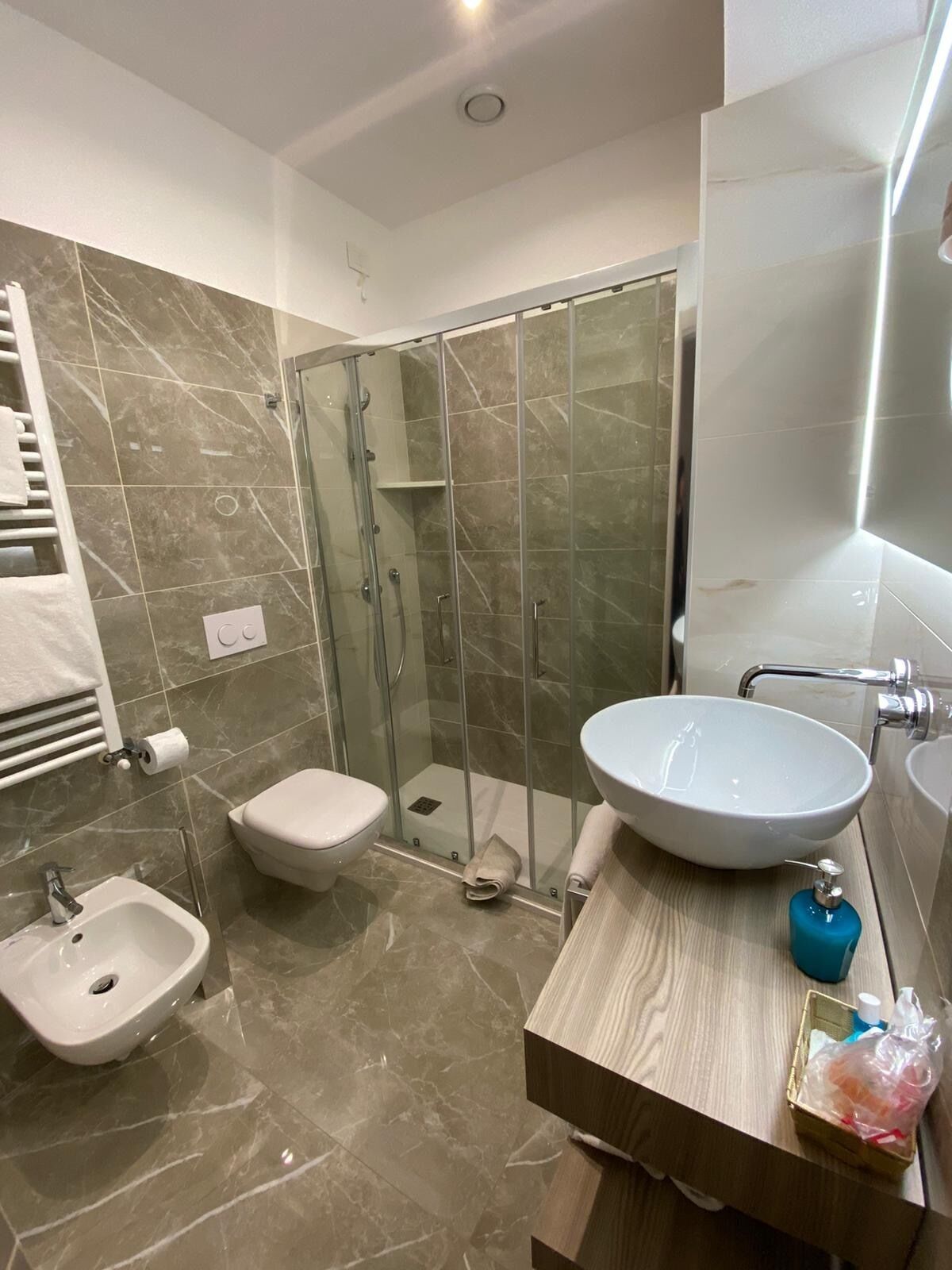 Et moderne badeværelse med en glasafskærmet brusekabine, et bidet, et toilet og en vaskebord med vask og spejl.
