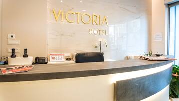 Un comptoir d’accueil à l’hôtel Victoria, avec un mur en marbre, un fauteuil en cuir noir, une plante et un magazine.