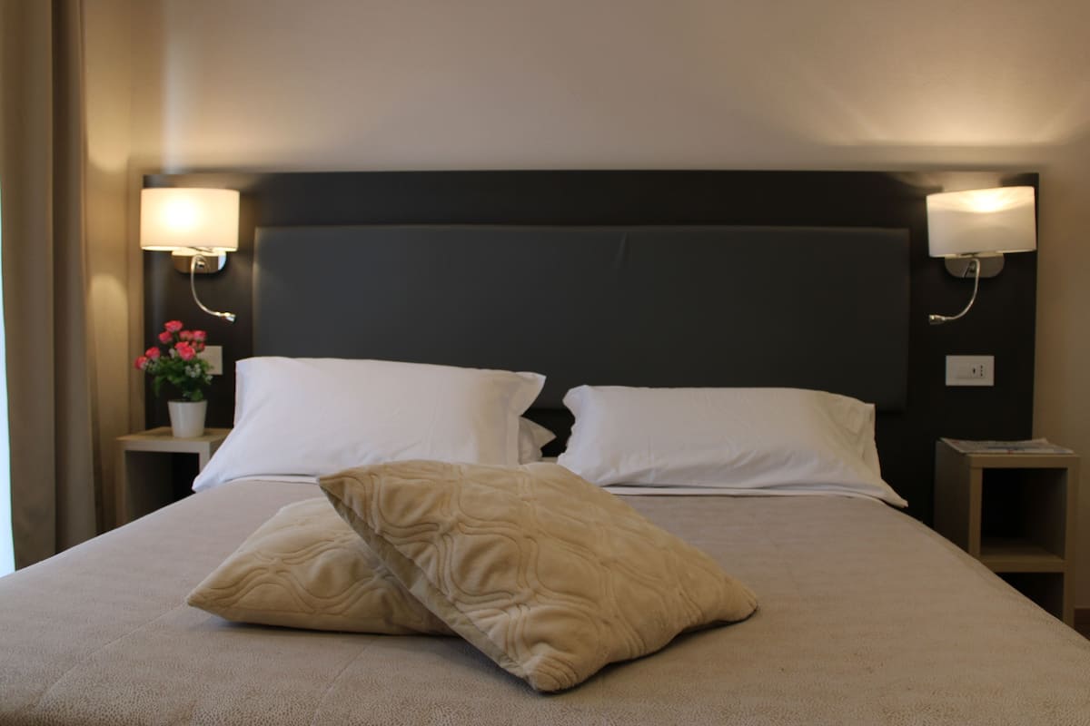 A neatly made bed with two pillows, a bedside table with a lamp, and a small nightstand with a lamp.