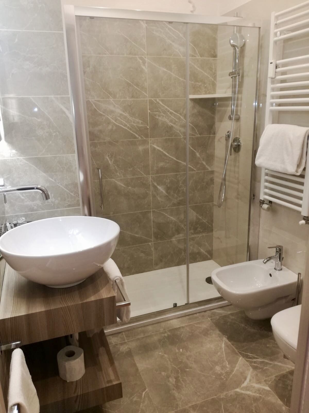 Une salle de bain avec un grand lavabo blanc, une douche à parois de verre, un bidet et un porte-serviettes.