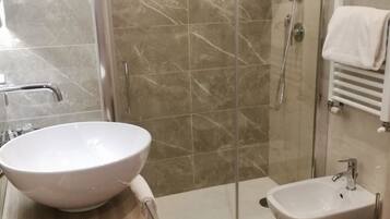 Une salle de bain avec un grand lavabo blanc, une douche à parois de verre, un bidet et un porte-serviettes.