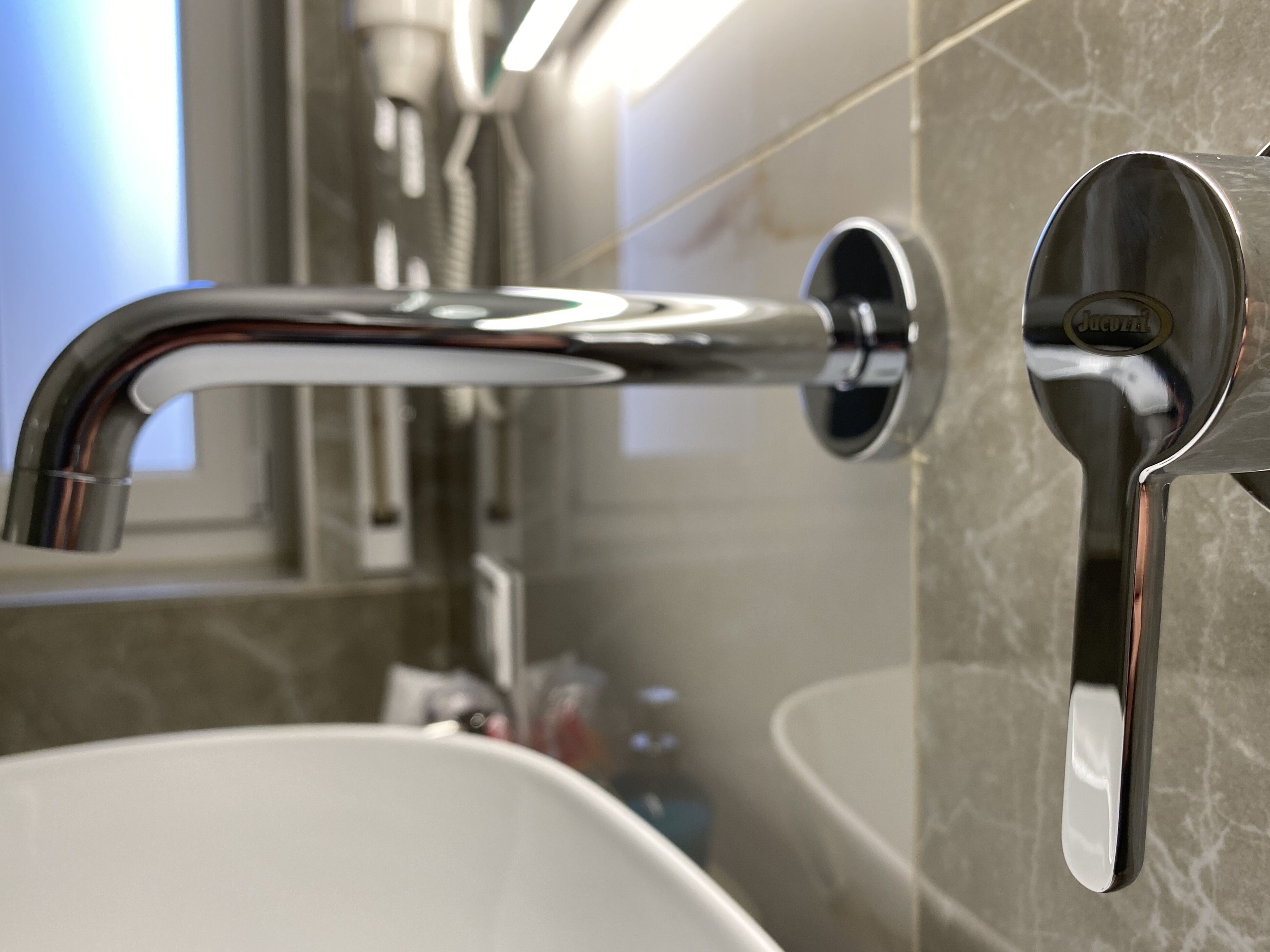 Un baño moderno con grifo de cromo, lavamanos blanco y pared de mármol.