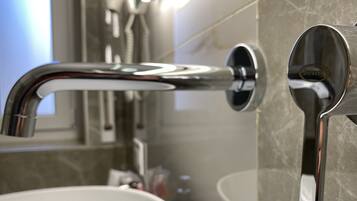 Un baño moderno con grifo de cromo, lavamanos blanco y pared de mármol.