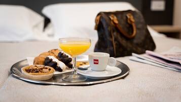 A breakfast tray with a croissant, a muffin, a glass of orange juice, and a cup of coffee on a hotel bed.
