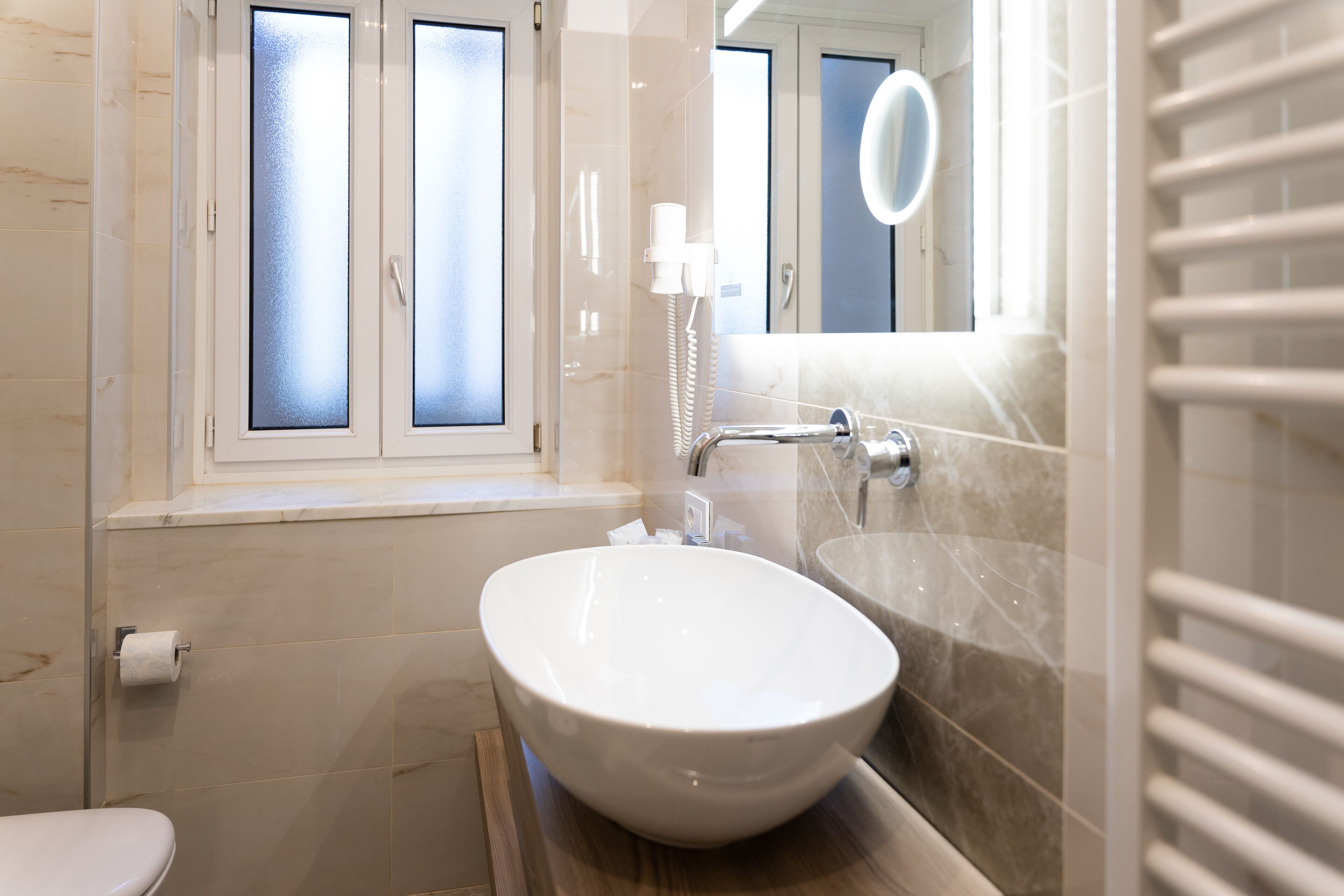 Un baño con un lavamanos blanco, un espejo y una ventana con vidrio esmerilado.