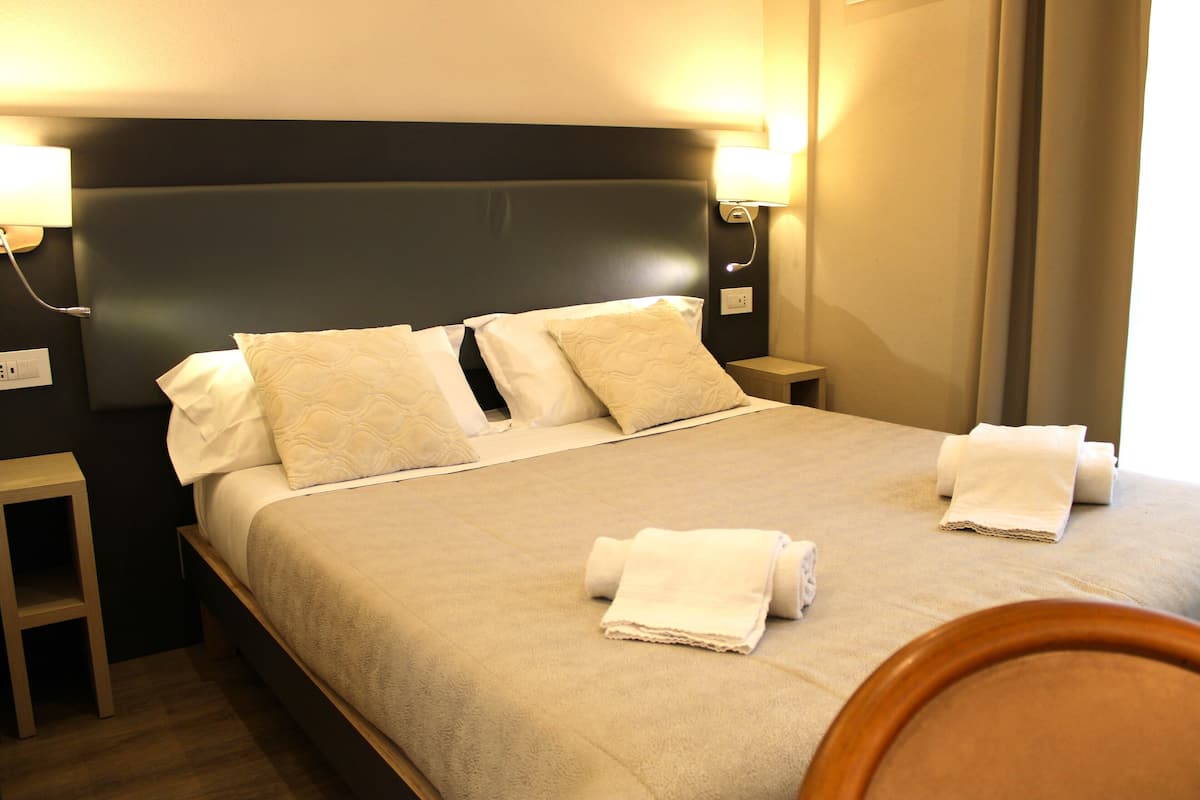 A neatly made bed with white linens and two rolled towels on the bed.