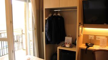 Ein Hotelzimmer mit einem Bett, einem Schreibtisch mit Fernseher, einem Kleiderständer mit Jacken und einem kleinen Kühlschrank.