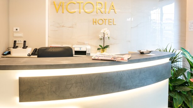 Un mostrador de recepción de hotel con pared de mármol, un mostrador, un teléfono, una impresora y una planta.