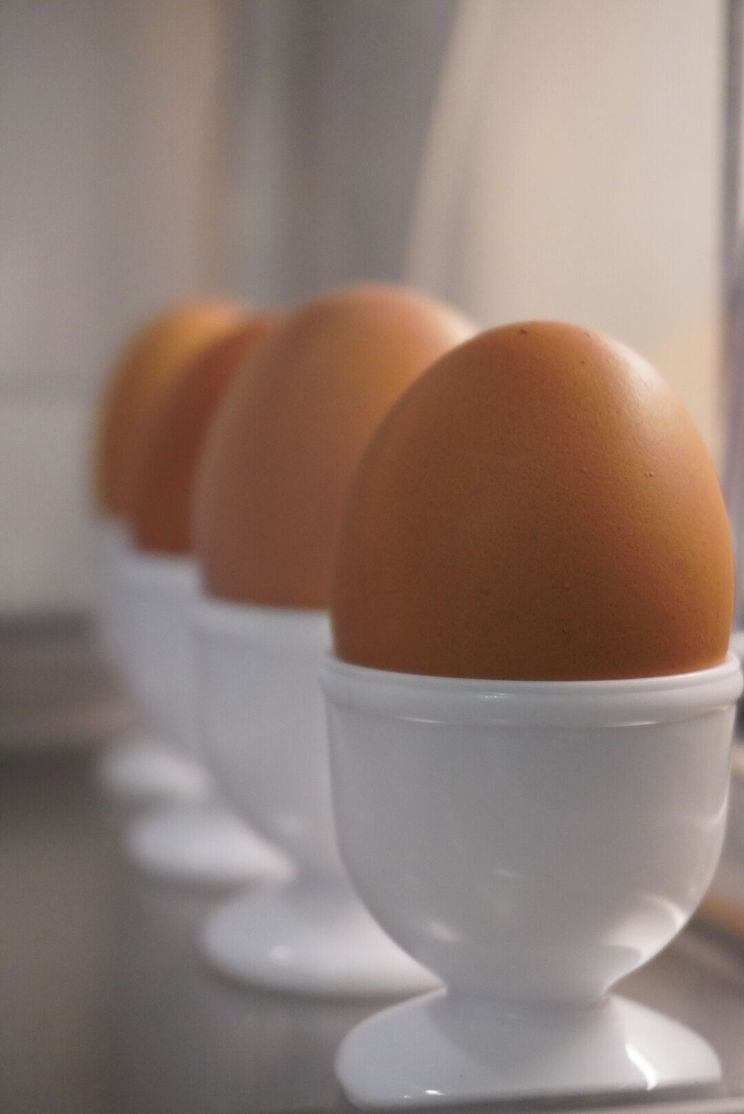 A row of white egg cups with brown eggs in them.