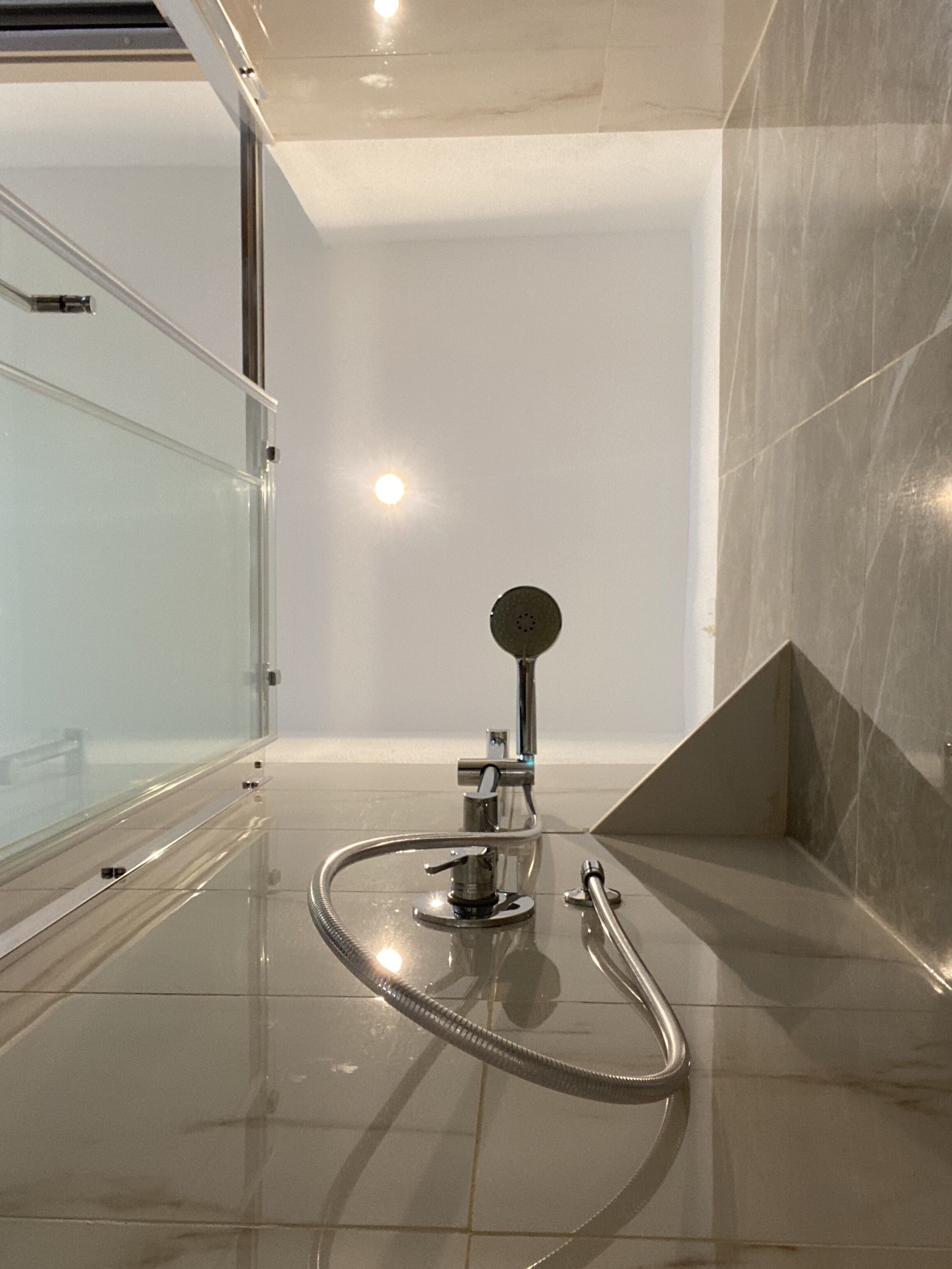 A modern bathroom with a glass shower enclosure, a handheld showerhead, and a floor-mounted faucet.