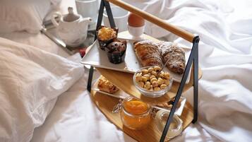 Bandeja de desayuno con pasteles, nueces y un frasco de mermelada sobre una cama con sábanas blancas.