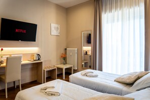 A hotel room with two beds, a desk, a TV displaying 'NETFLIX', a radiator, and a window with curtains. - Hotel Victoria (Cuneo)