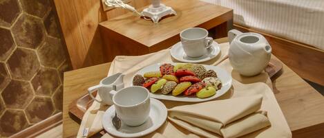 Bandeja de café da manhã bem organizada com pães, um bule, xícaras e um jarro pequeno sobre uma mesa de madeira em um quarto de hotel.