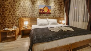A hotel room with a large bed, two bedside tables with lamps, a painting of hot air balloons, and a view of the city through sheer curtains. - Newway Hotel (Kocasinan)