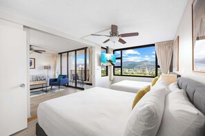 Ein Hotelzimmer mit zwei Betten, einem Deckenventilator, einem Fernseher, einem Balkon mit Stadtblick und einem Schreibtisch mit Stuhl.