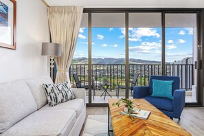 A modern living room with a sofa, a blue armchair, a wooden coffee table, and a view of mountains through large glass doors.